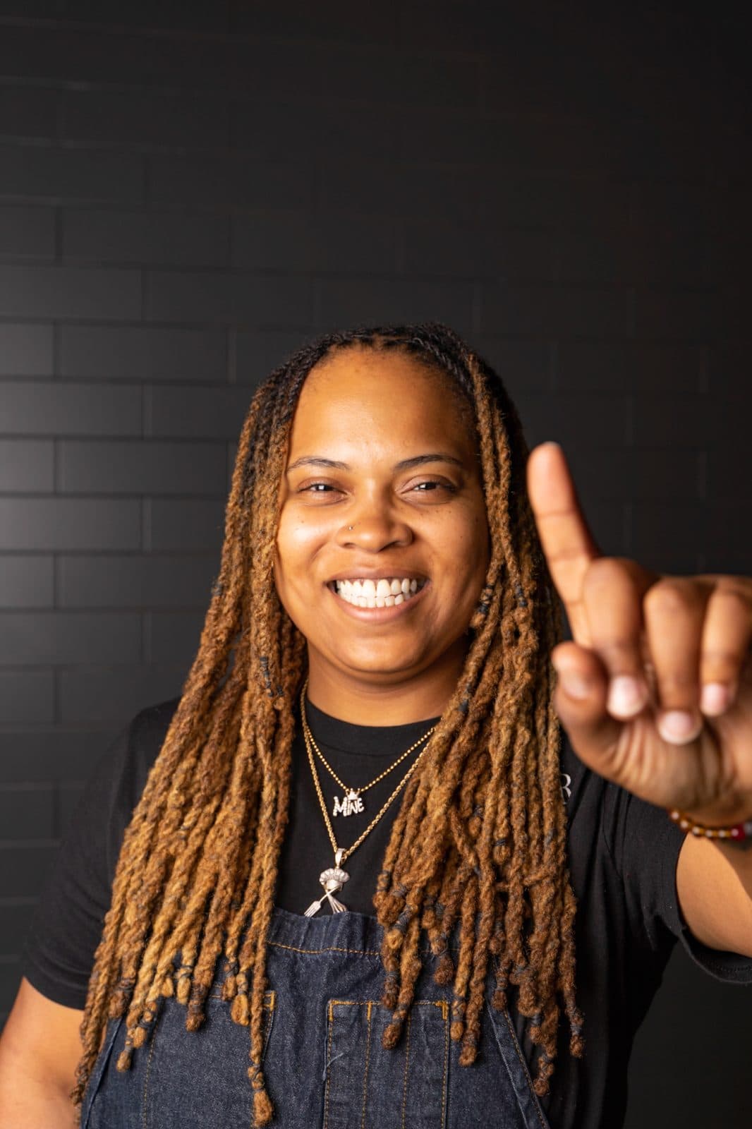 woman holding a finger up in front of brick wall