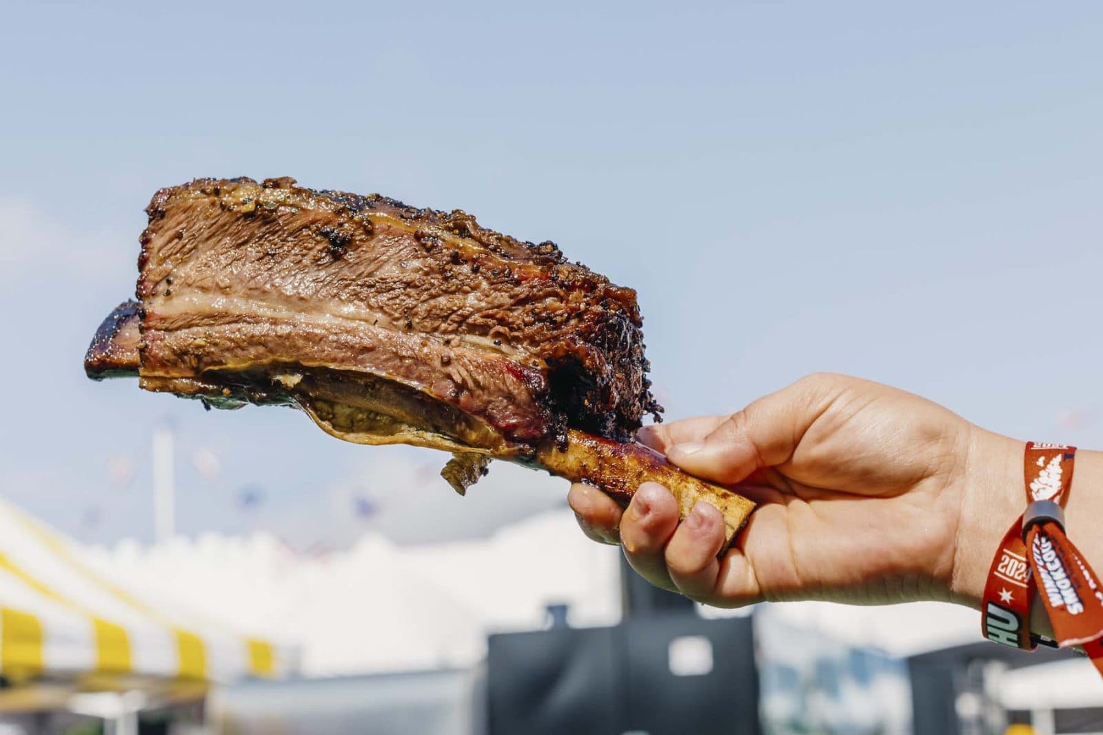 a hand holding a large single beef rib in the air
