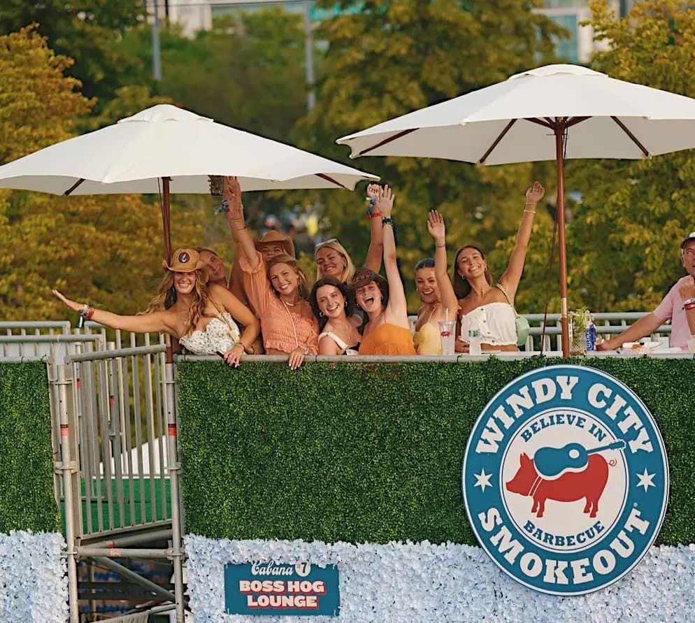 a group of concert goers waving to the camera from atop a concert cabana
